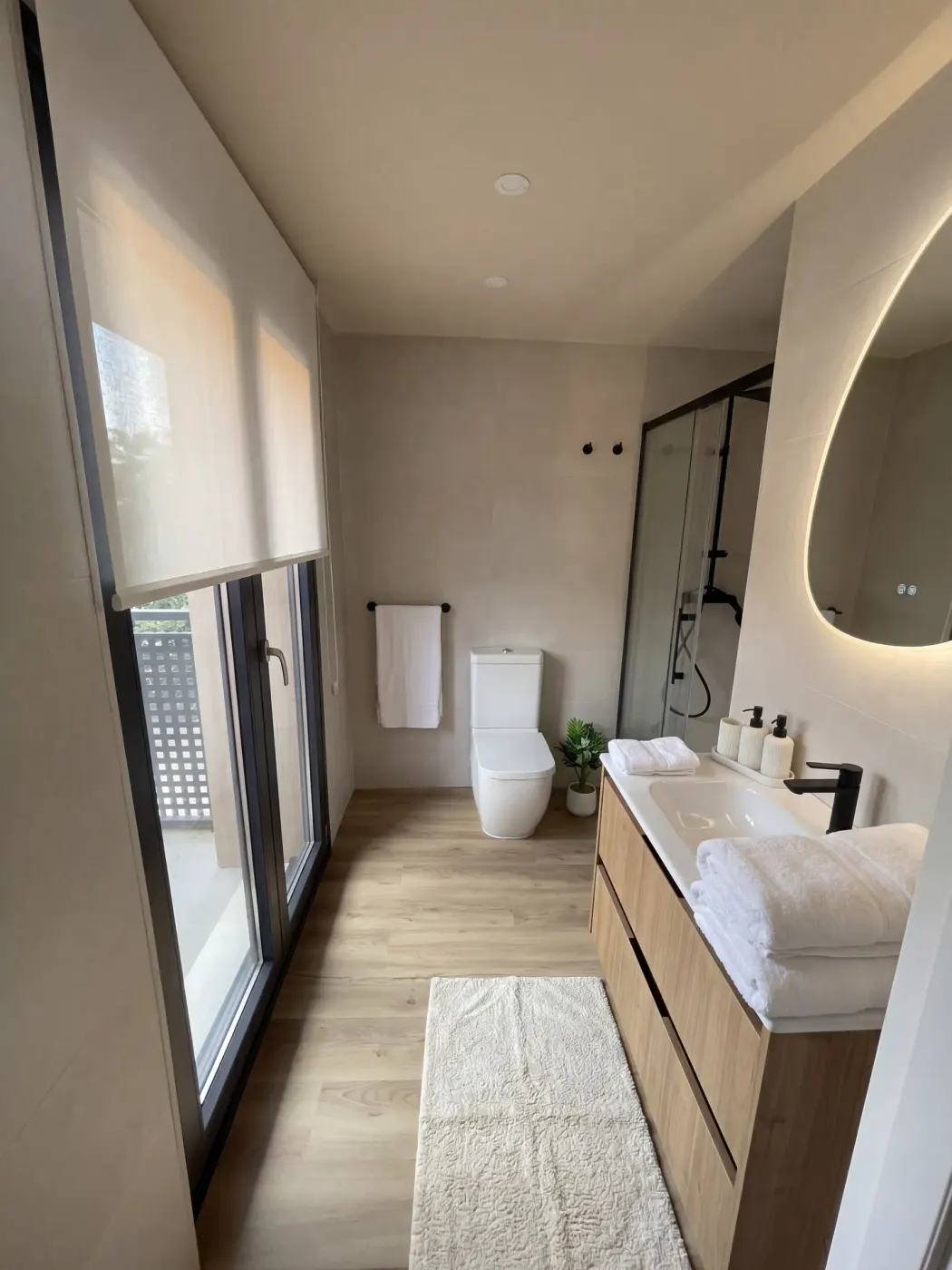 Baño del hotel con ducha, espejo retroiluminado y mueble de madera