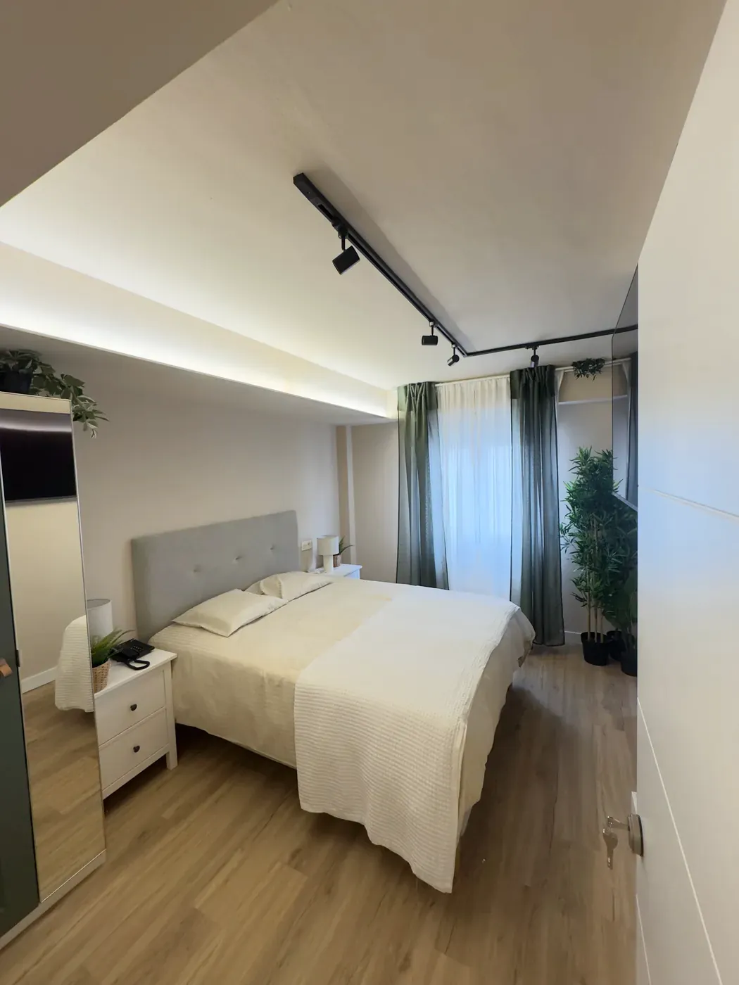 Cama de la habitación doble, con cortinas verdes junto a la ventana