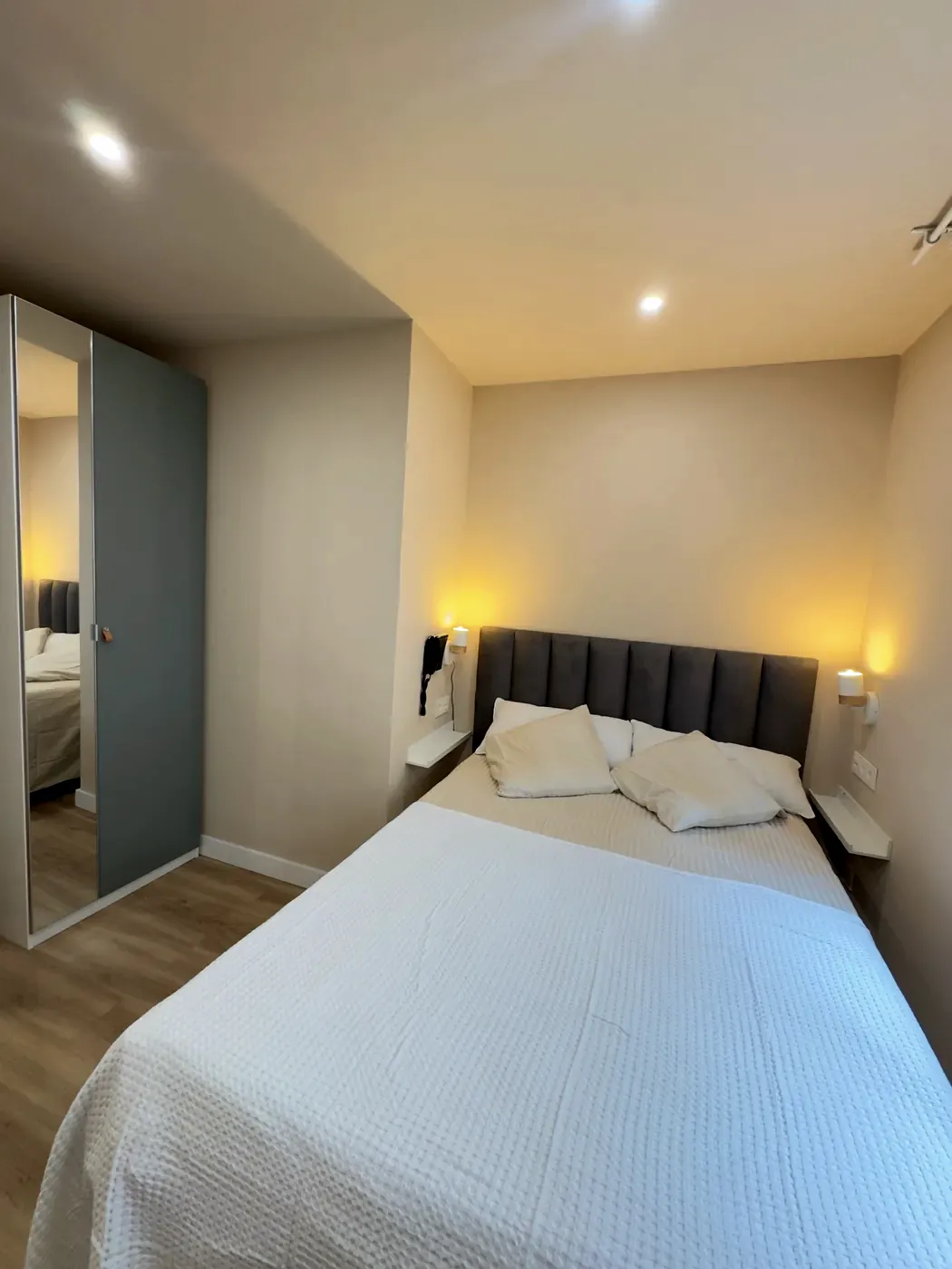 Cama de matrimonio con cabecero tapizado y lámparas de lectura