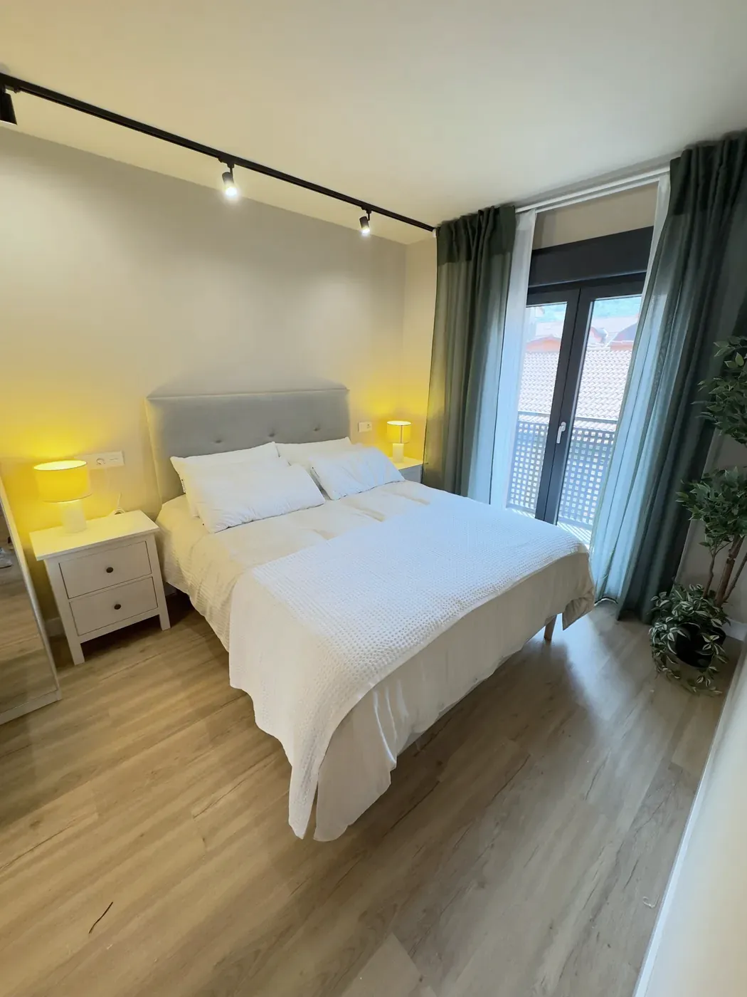 Dormitorio de la suite con cama Queen Size, lámparas encendidas y cortinas verdes